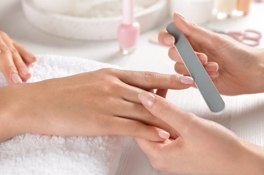 Manicurist filing client's nails at table, closeup. Spa treatment