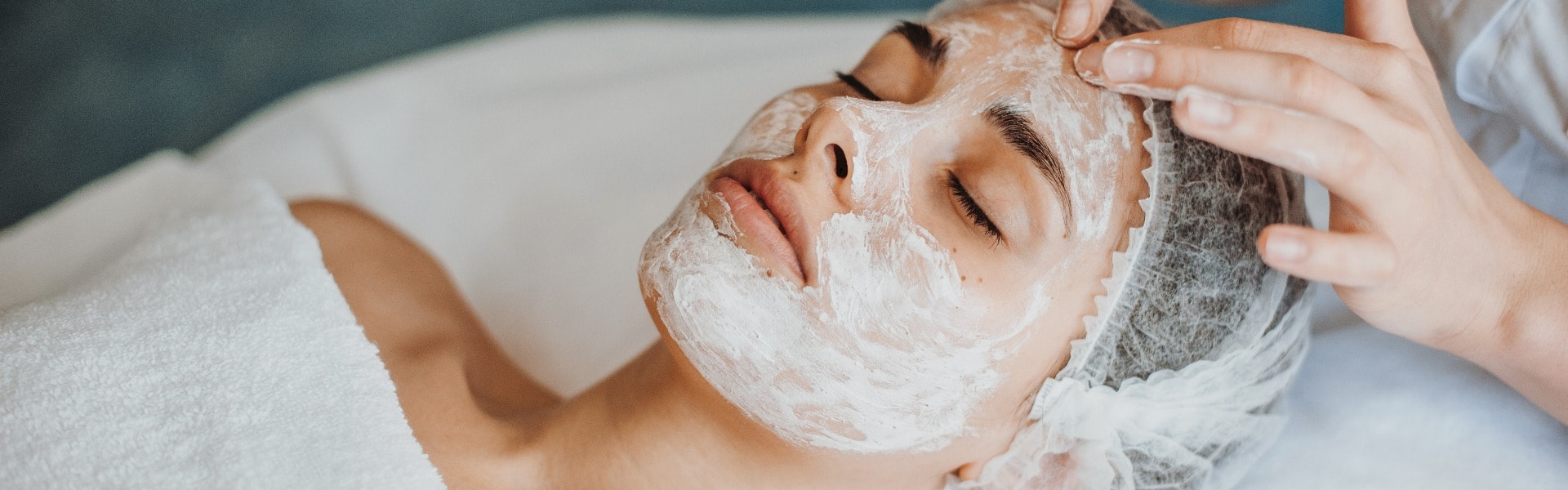 Woman face getting facial care with cream by beautician hands at spa salon. Close-up portrait.